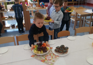 chłopcy roznoszą talerze z owocami